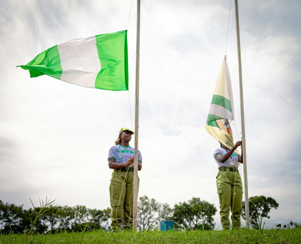 Two youth corps members participate in a flag-raising ceremony outdoors in Kaduna, Nigeria.