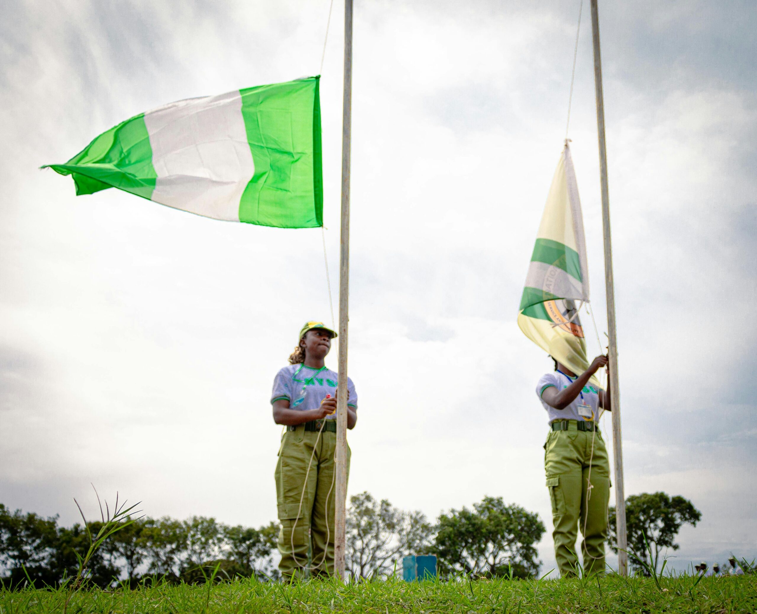 Two youth corps members participate in a flag-raising ceremony outdoors in Kaduna, Nigeria.