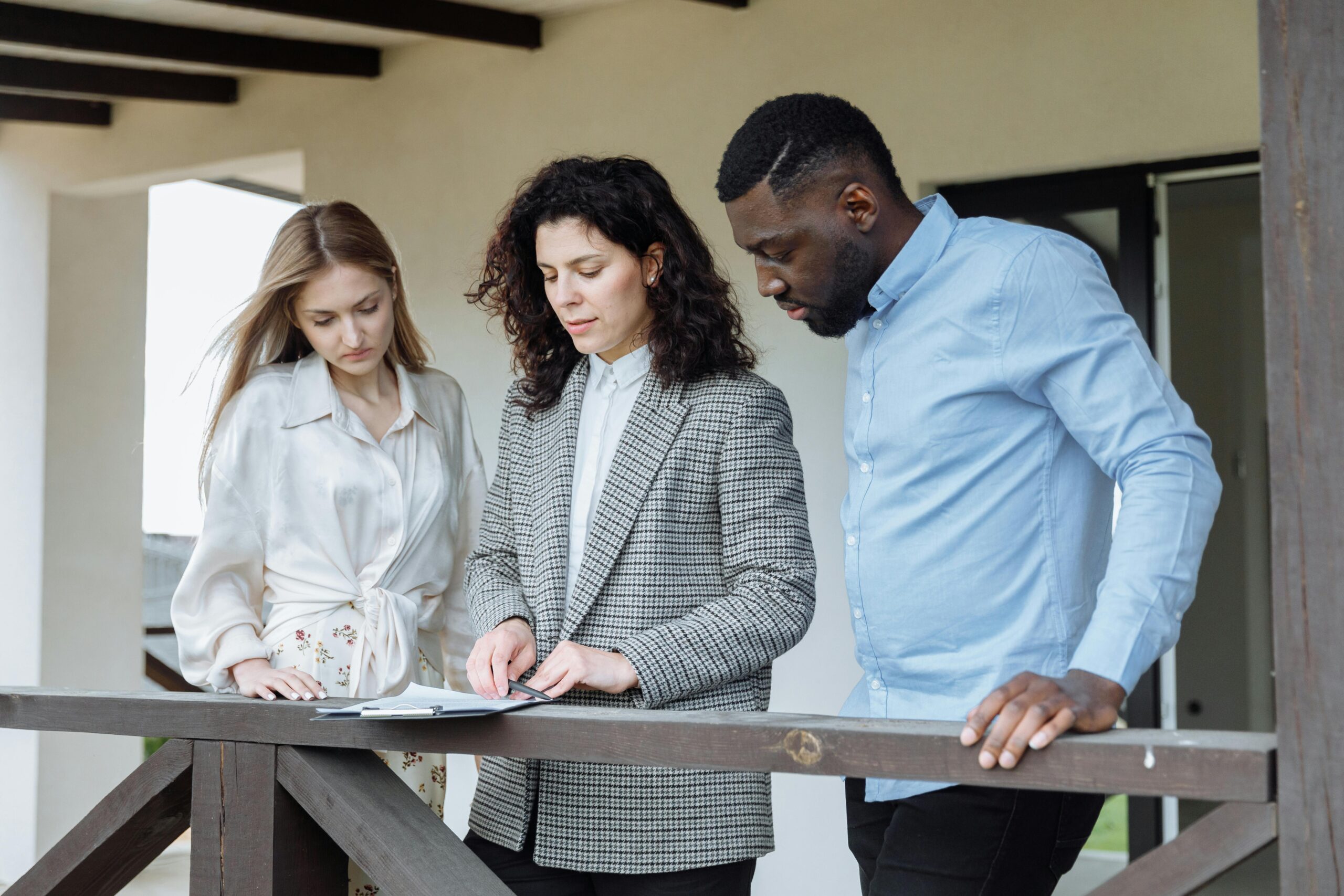 Three adults reviewing documents on a balcony during a real estate consultation.